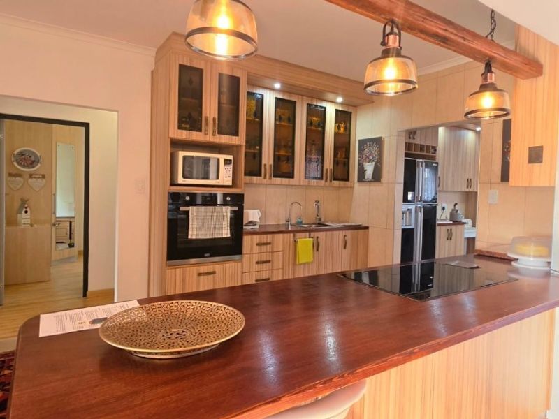 A well-maintained kitchen featuring wood-finish cabinetry, a built-in oven and microwave, a sleek hob, and a spacious wooden breakfast island with pendant lighting.