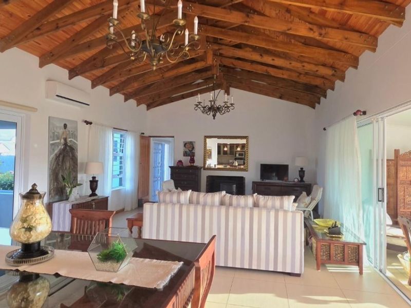 Spacious open-plan living and dining area featuring a vaulted timber beam ceiling, fireplace, and large sliding glass doors leading to an outdoor space.