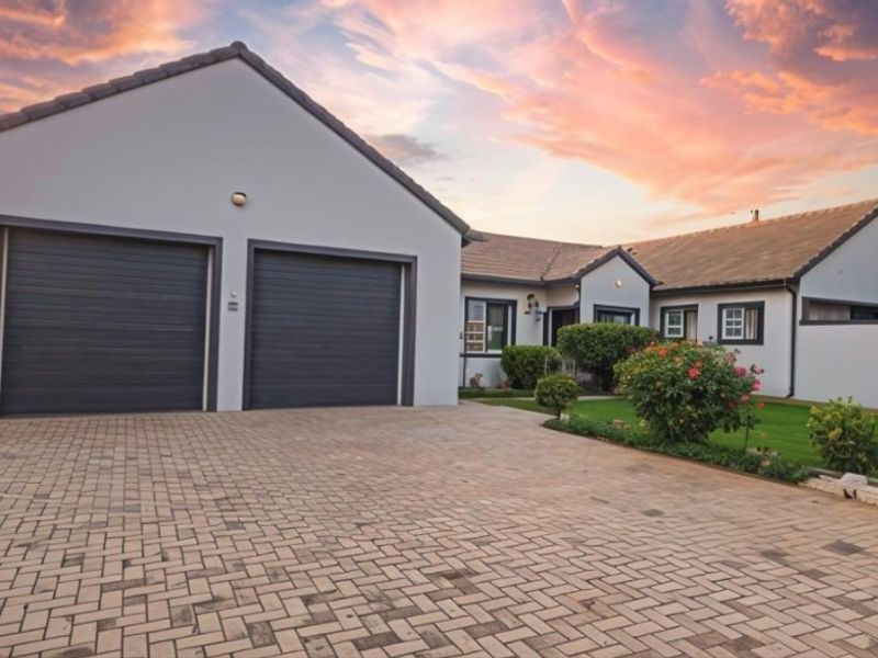 A well-maintained front exterior featuring a paved driveway, double garage, and neat lawn area under a sunset sky.