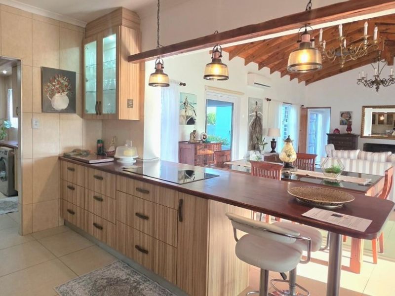 Spacious open-plan kitchen and living area featuring timber cabinetry, a breakfast bar, exposed ceiling beams, and seamless flow to the adjacent living space.