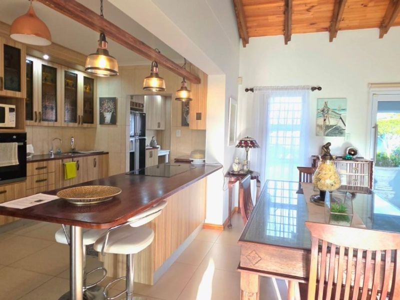 Spacious open-plan kitchen and dining area featuring modern cabinetry, a breakfast island, and exposed timber ceiling beams with direct access to the patio.