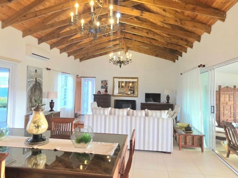 Spacious open-plan living and dining area featuring a high vaulted timber ceiling, tiled floors, and large sliding doors leading to an outdoor space.