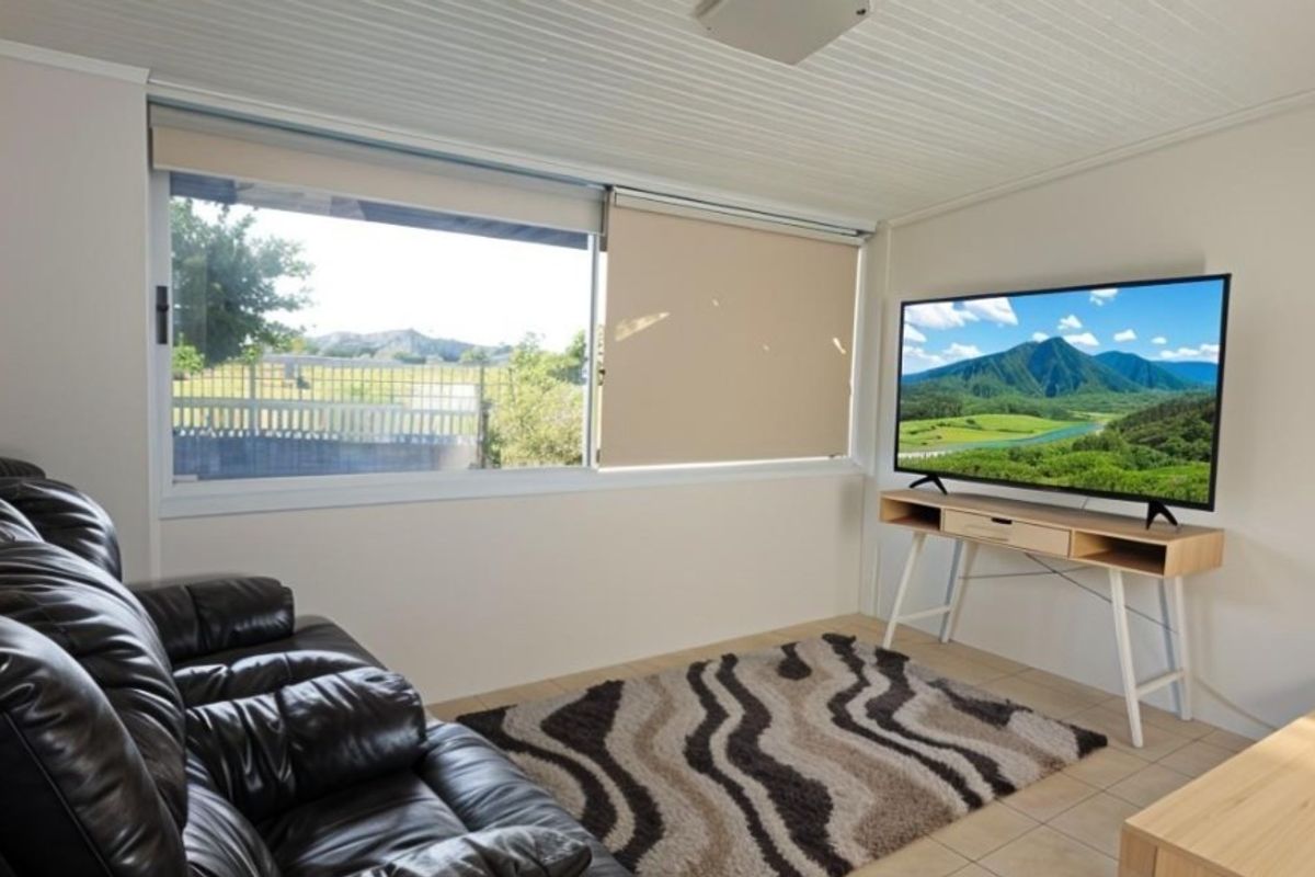 A bright living room featuring tiled flooring, a large sliding window with roller blinds, and a tongue and groove ceiling.