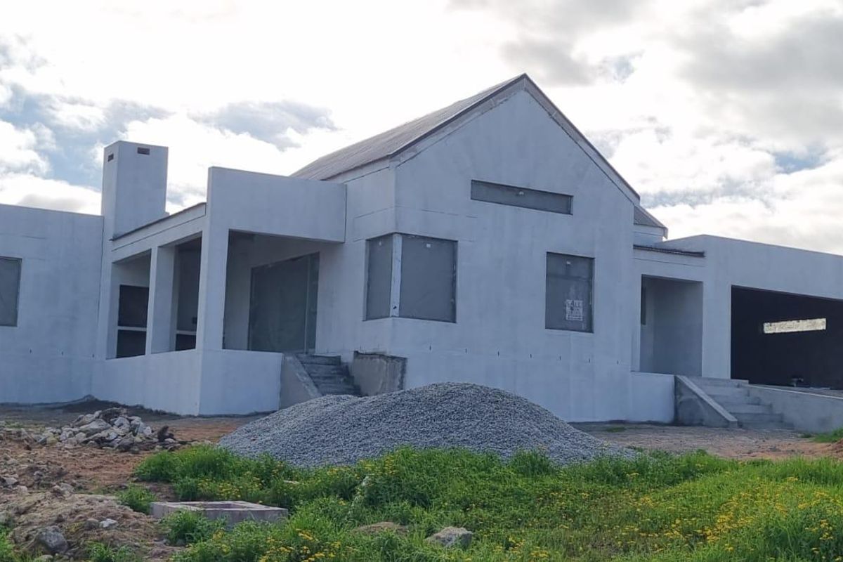 A newly constructed house in the final stages of building, featuring a modern facade, chimney, and integrated garage, currently awaiting final exterior finishing.