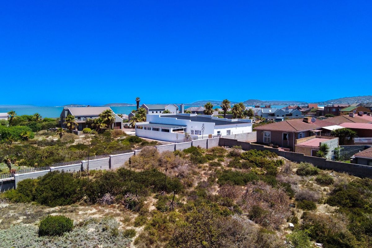 An aerial view of the property showing the surrounding coastal landscape, boundary walls, and neighboring residential homes.