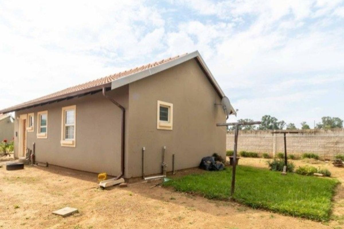 A view of the rear exterior of the house, featuring a tiled roof, plastered walls, and a simple garden area with a clothesline.
