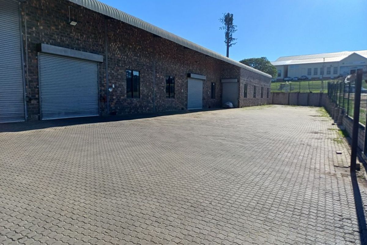 Industrial property exterior featuring a large paved yard area, brick facade, and multiple roller shutter doors for efficient access.