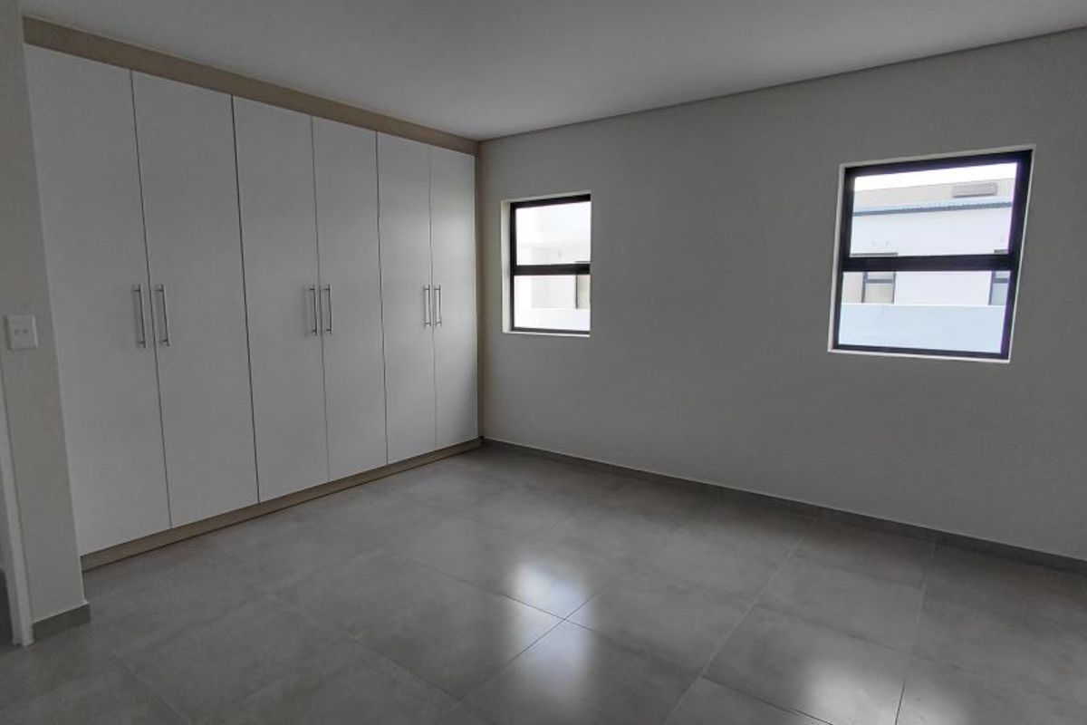 A bright, modern bedroom featuring large-format floor tiles and extensive built-in cabinetry with sleek handles.