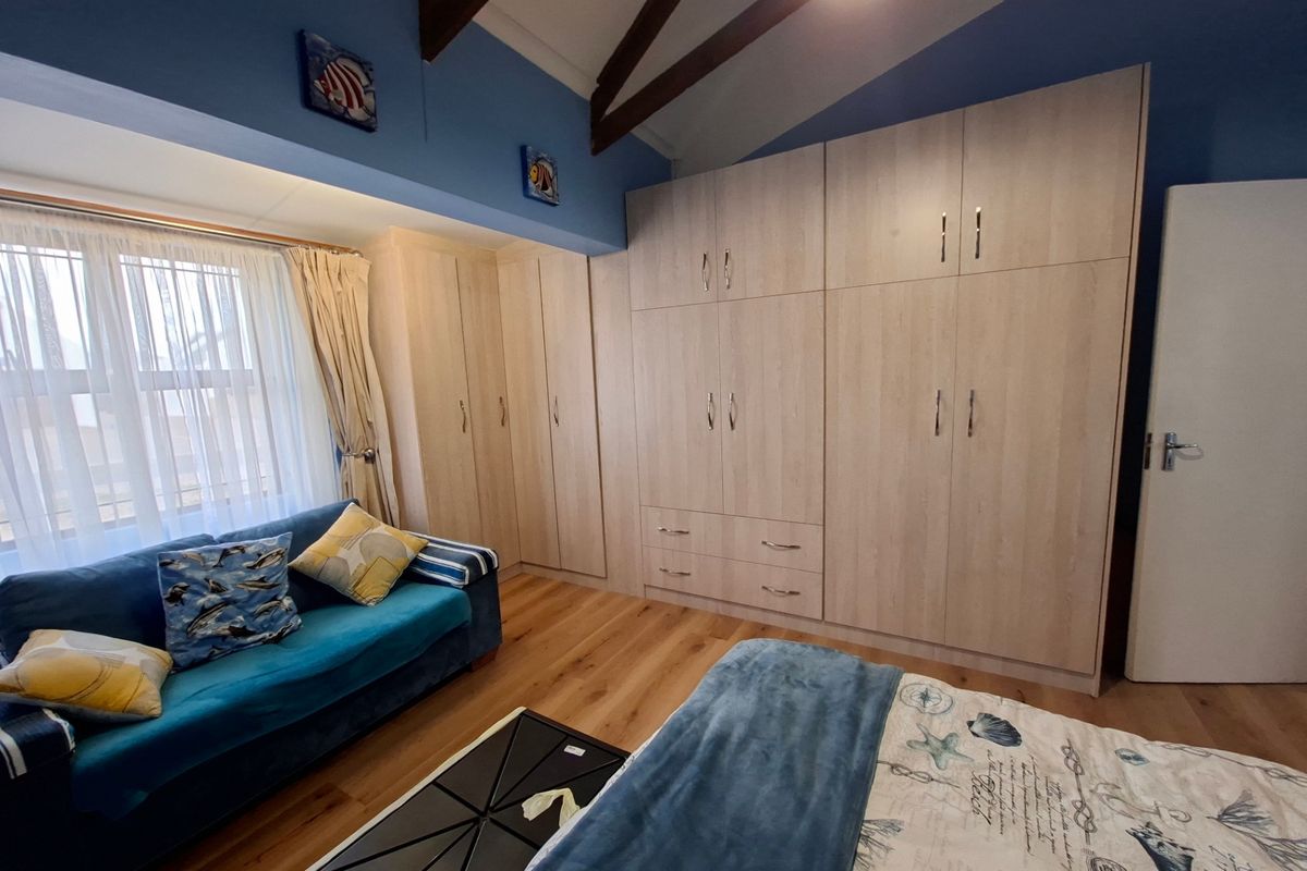 A well-maintained bedroom featuring extensive built-in cabinetry, exposed timber ceiling beams, and durable laminate flooring.