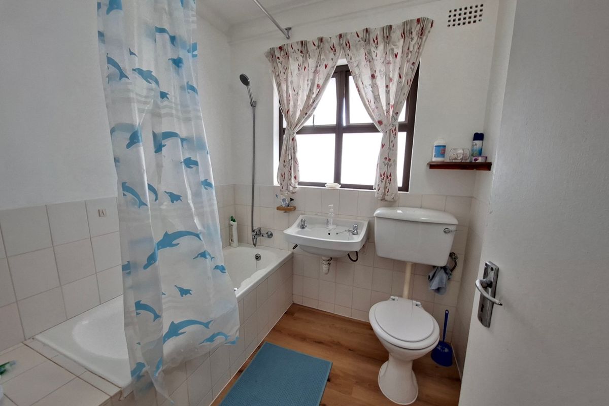 A functional bathroom featuring a built-in bathtub with shower attachment, wall-mounted basin, and a standard toilet with laminate flooring.