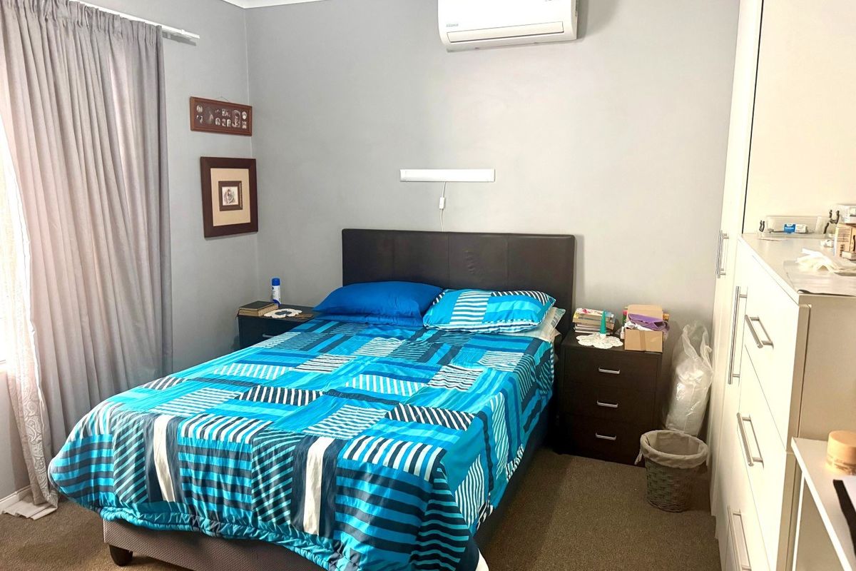 A functional bedroom featuring carpet flooring, a built-in wardrobe, and a wall-mounted split-system air conditioner for climate control.