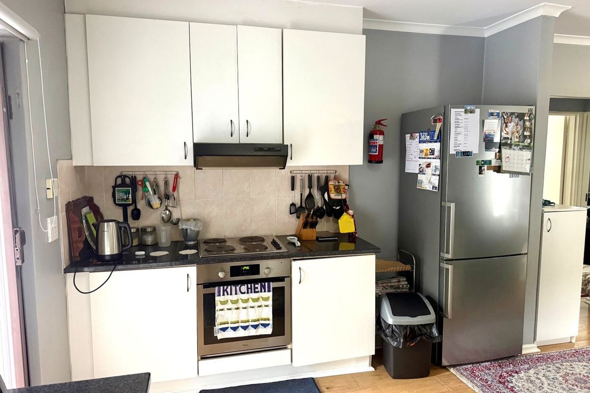 A functional kitchen featuring white cabinetry, dark countertops, a built-in oven with electric hob, and a tiled splashback.
