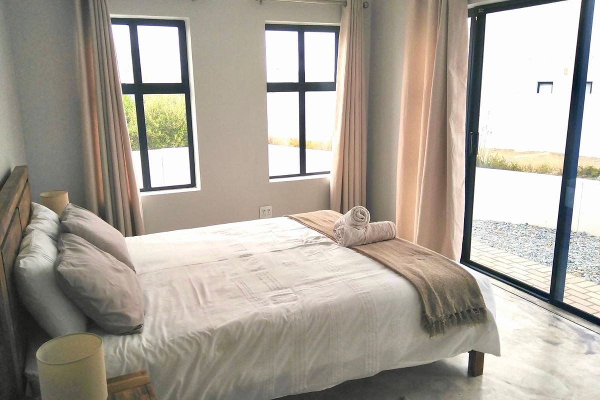 A bright bedroom featuring polished concrete floors, modern aluminium window frames, and a sliding glass door providing direct access to the outdoor area.