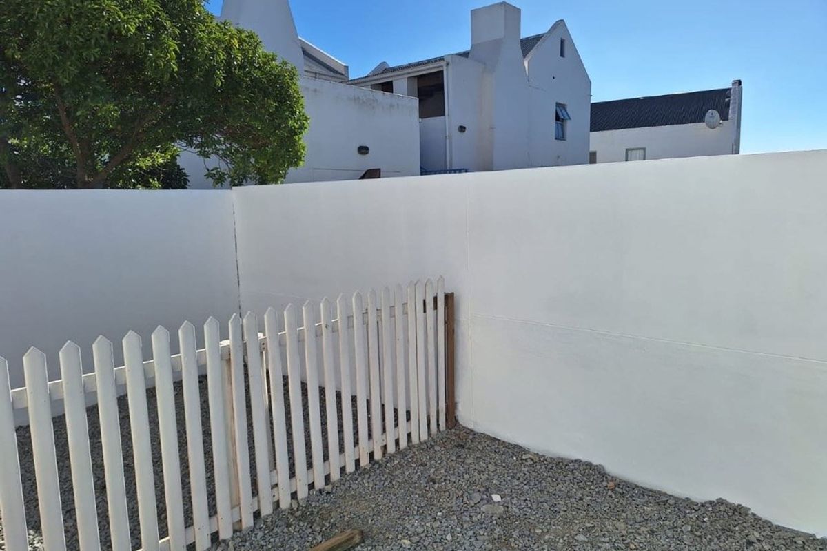 A private rear courtyard area featuring a white boundary wall, a picket fence, and gravel ground cover.