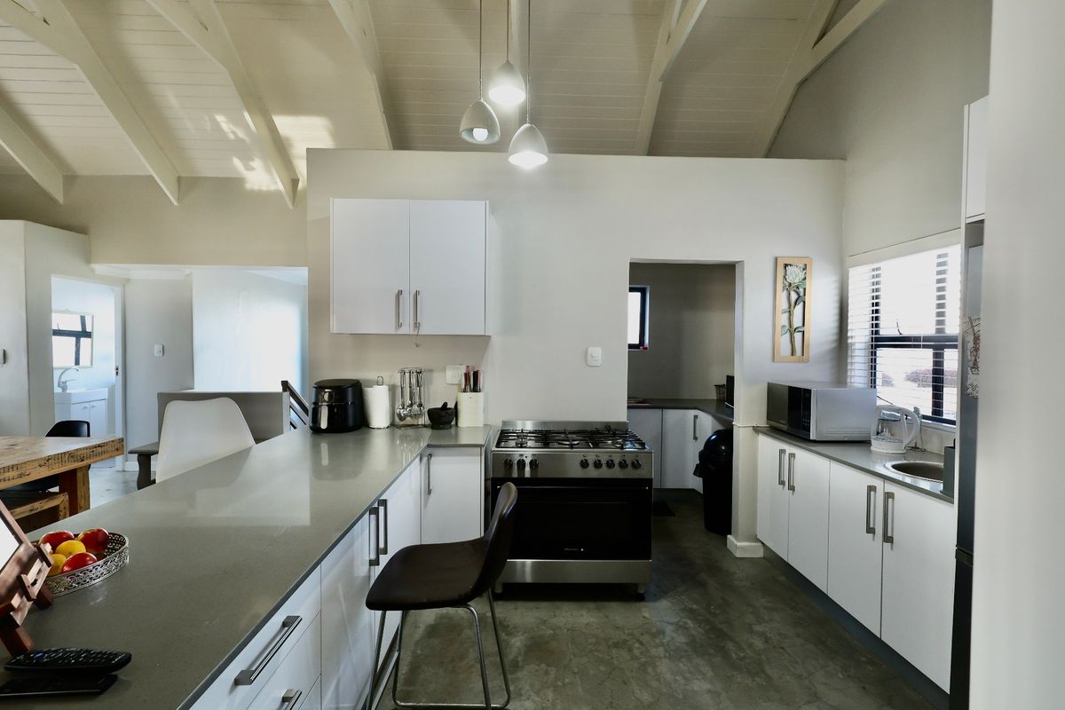 Modern kitchen featuring white cabinetry, stone countertops, gas stove, and high vaulted ceilings with exposed beams, creating a bright and open culinary space.