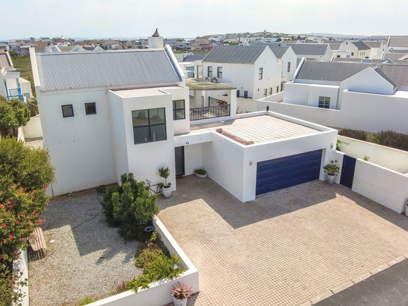 Aerial view of a modern white house featuring a paved driveway, garage, and upper-level balcony in a coastal residential estate.