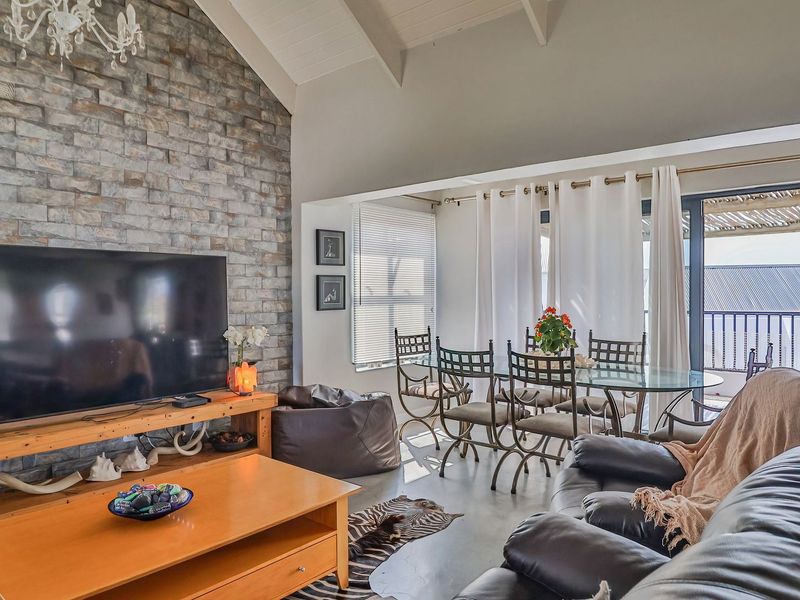 Spacious open-plan living and dining area featuring a striking stone feature wall, vaulted ceilings with exposed rafters, and polished concrete flooring.