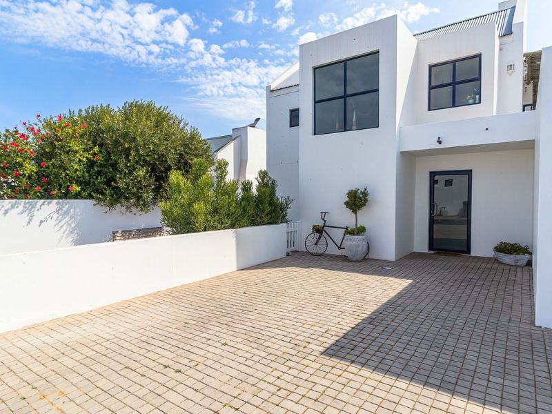 A modern white facade featuring a paved driveway, clean architectural lines, and a secure main entrance.