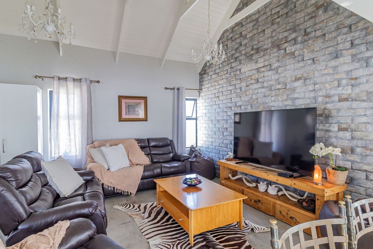 Spacious living room featuring a high vaulted ceiling with exposed rafters and a striking stone feature wall.