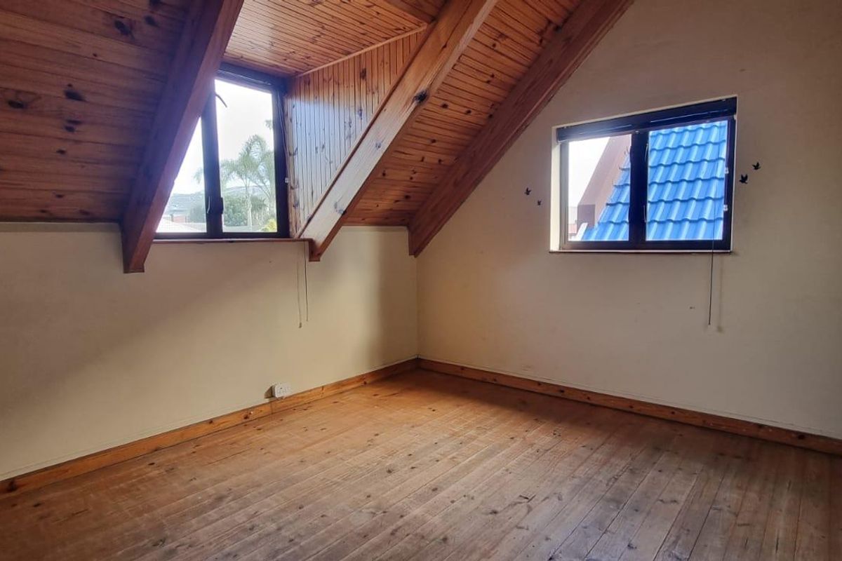An empty bedroom featuring a vaulted timber-clad ceiling, timber flooring, and built-in wardrobe storage, offering a cozy attic-style living space.