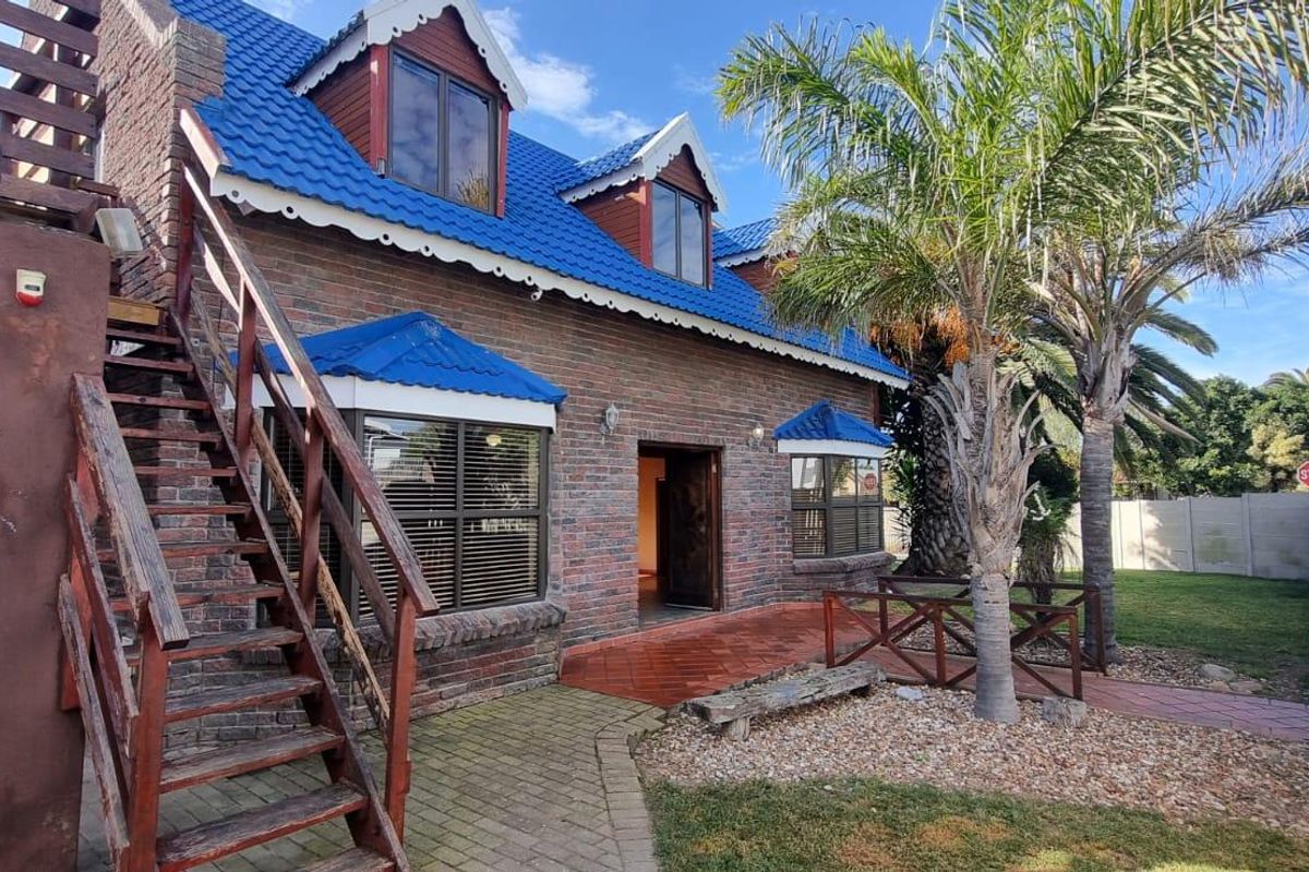 Rear view of a double-story brick house featuring a blue tiled roof, dormer windows, and an external timber staircase leading to an upper level.