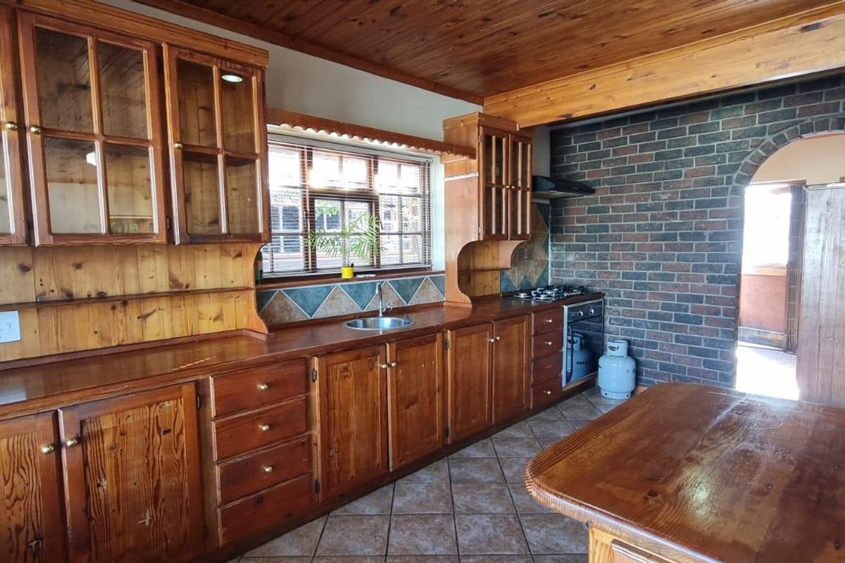 A rustic kitchen featuring extensive wooden cabinetry, exposed brickwork, a gas hob, and tiled flooring, offering a traditional aesthetic with potential for modernization.