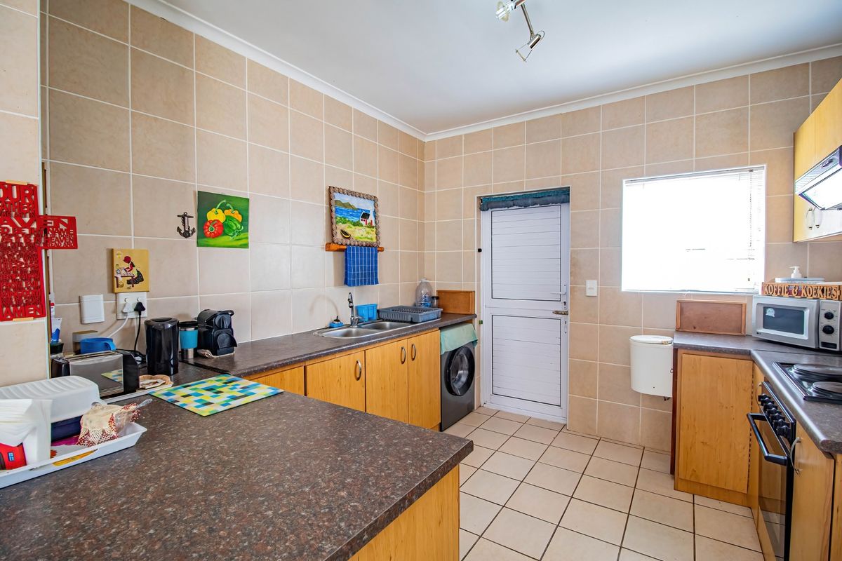 Functional kitchen featuring laminate cabinetry, tiled splashbacks, built-in oven and hob, and direct access to the exterior.