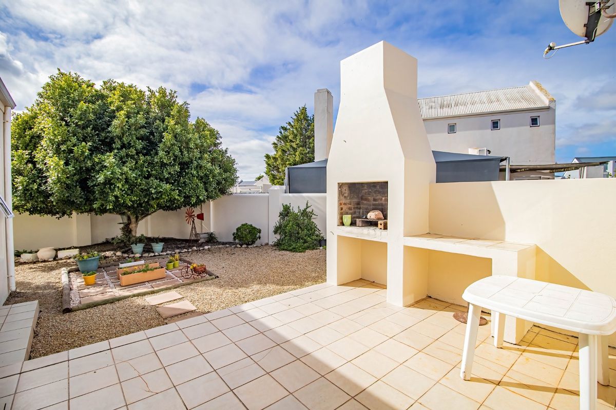 A private rear courtyard featuring a tiled patio area with a built-in braai, gravel landscaping, and perimeter boundary walls.