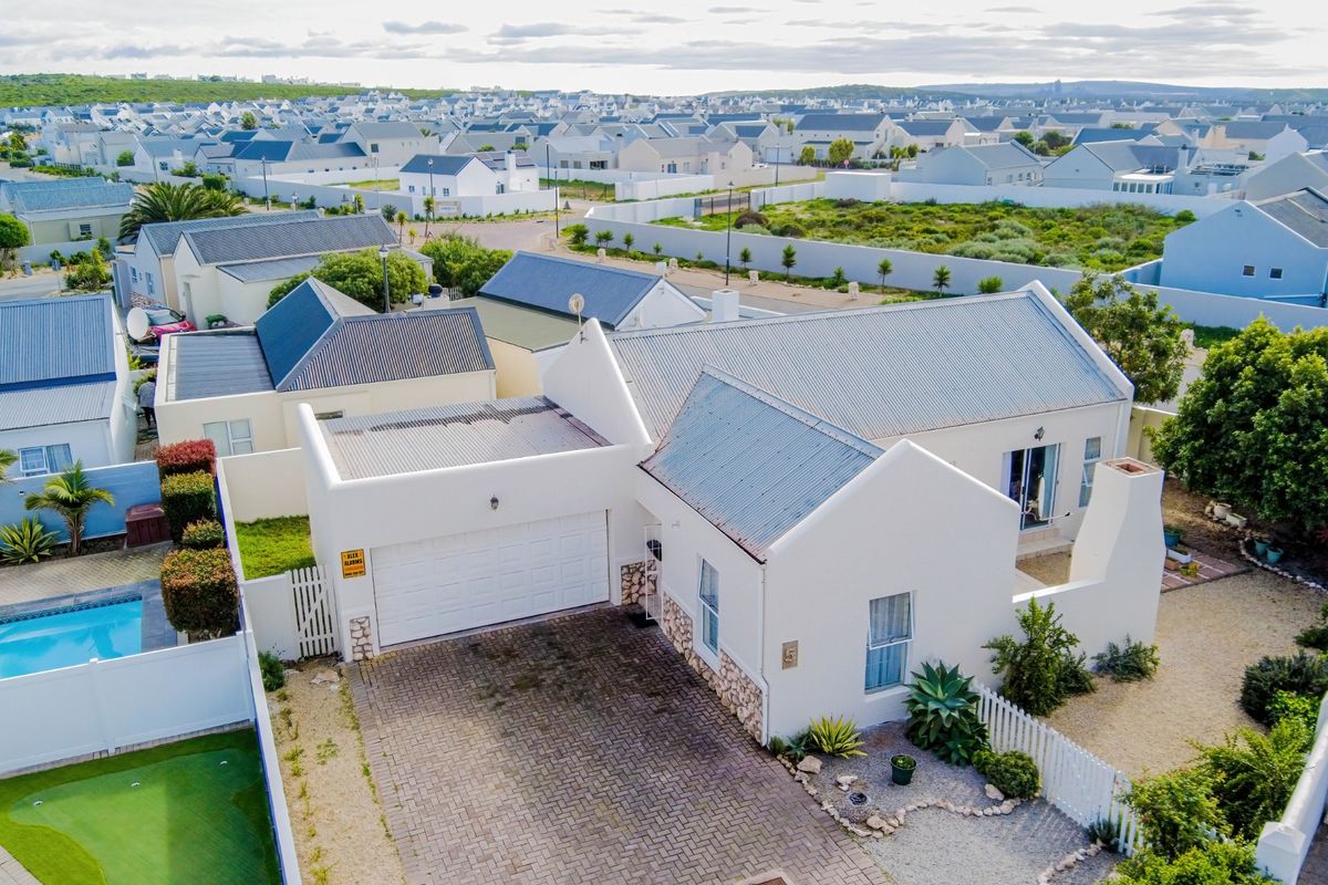 Aerial view of a residential property featuring a paved driveway, attached garage, corrugated metal roof, and a private swimming pool in a suburban estate.