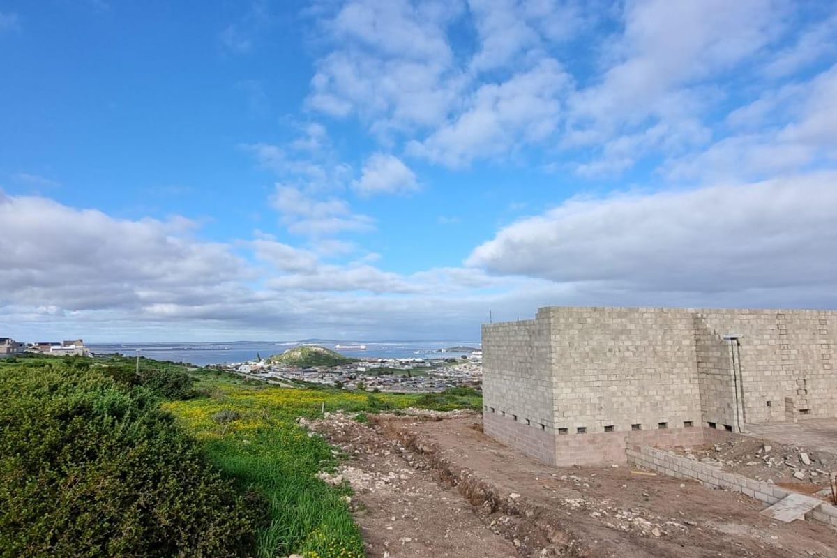 A construction site showing the exterior shell of a house under development with expansive coastal and landscape views.