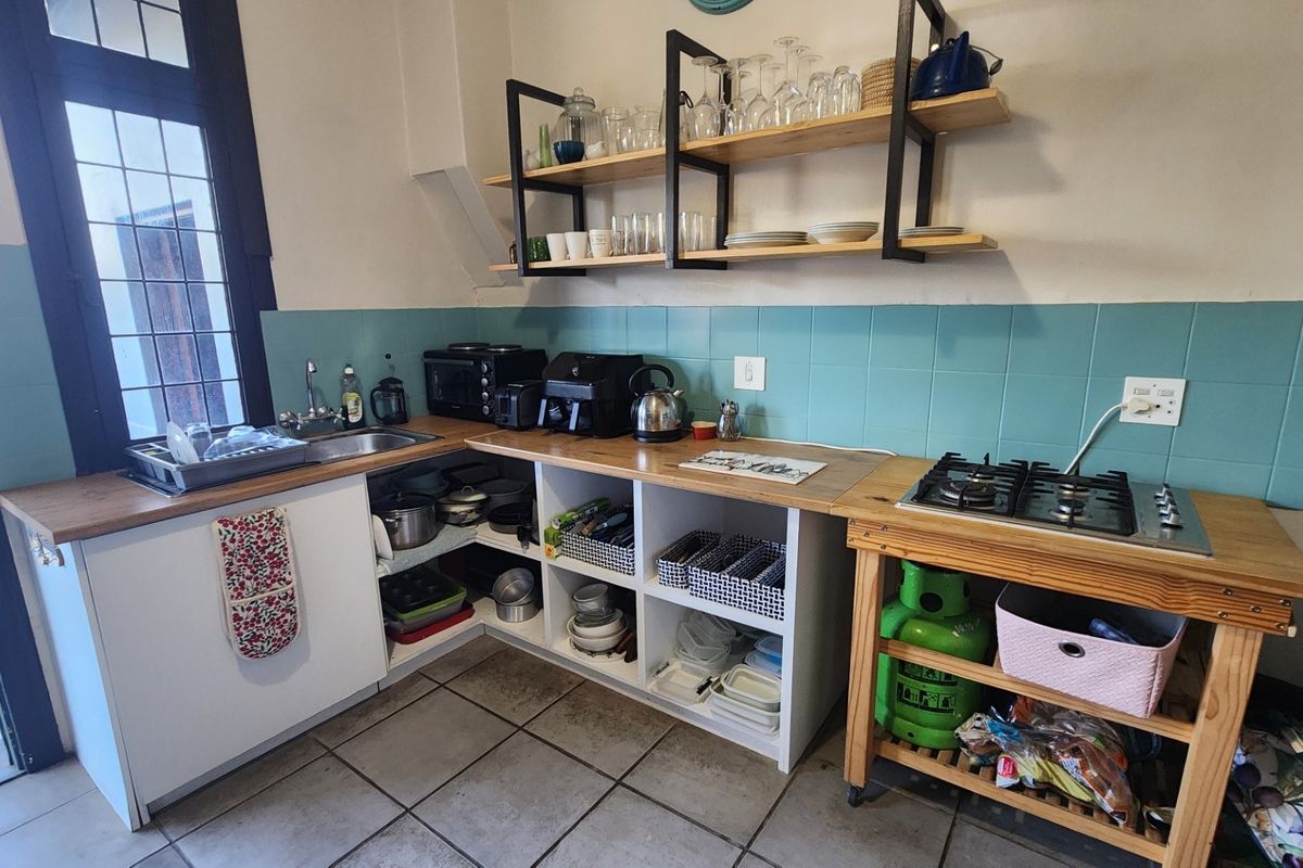 A functional kitchen area featuring a gas hob, tiled splashback, open shelving, and a built-in sink with tiled flooring.