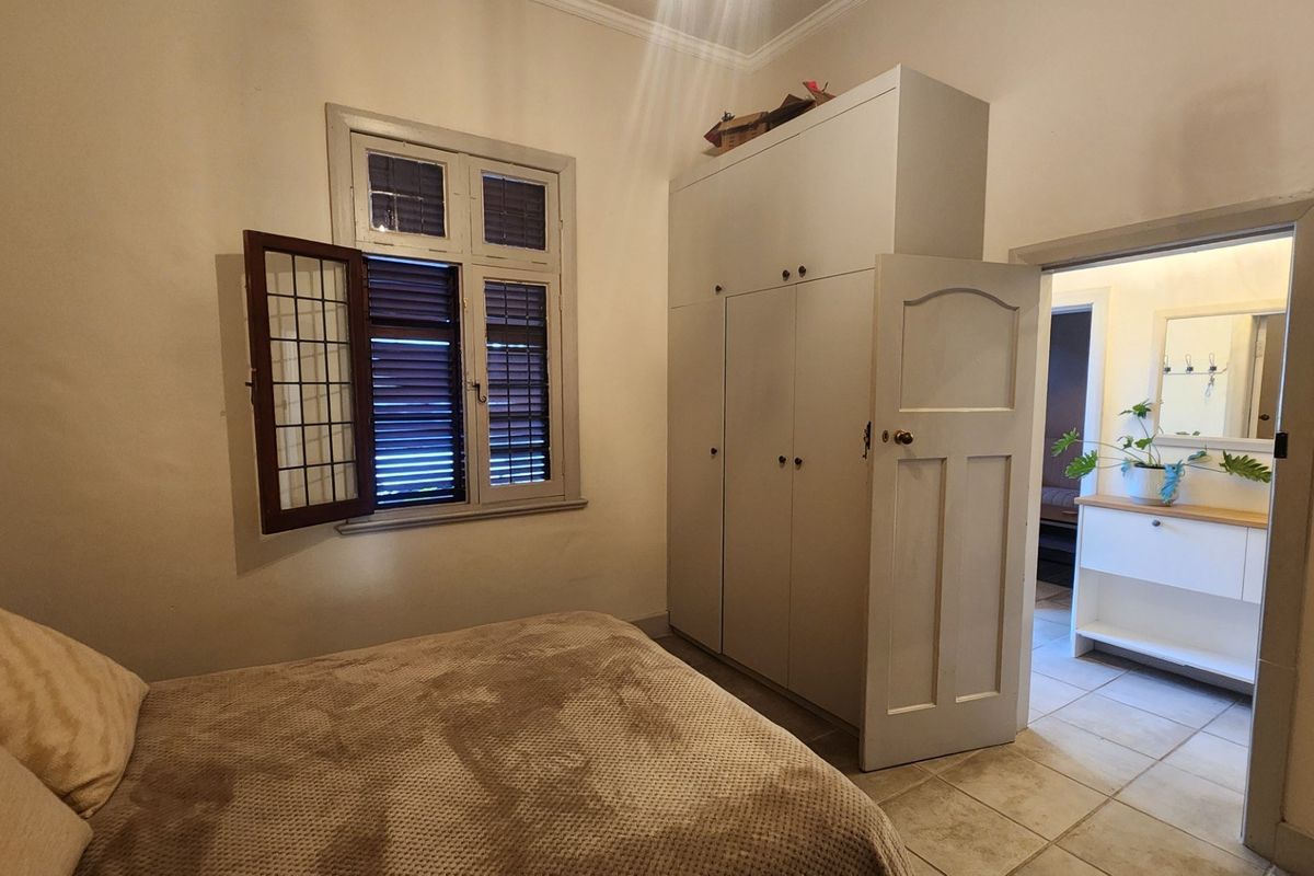 A bedroom featuring a built-in wardrobe, tiled flooring, and a casement window, with an adjacent view into a bathroom area.