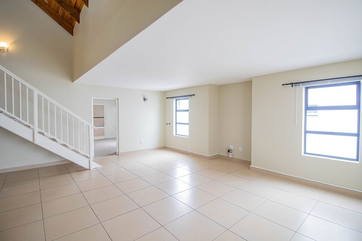 Spacious open-plan living area featuring neutral tiled flooring, a feature staircase with white balustrade, and high ceilings with exposed timber beams.