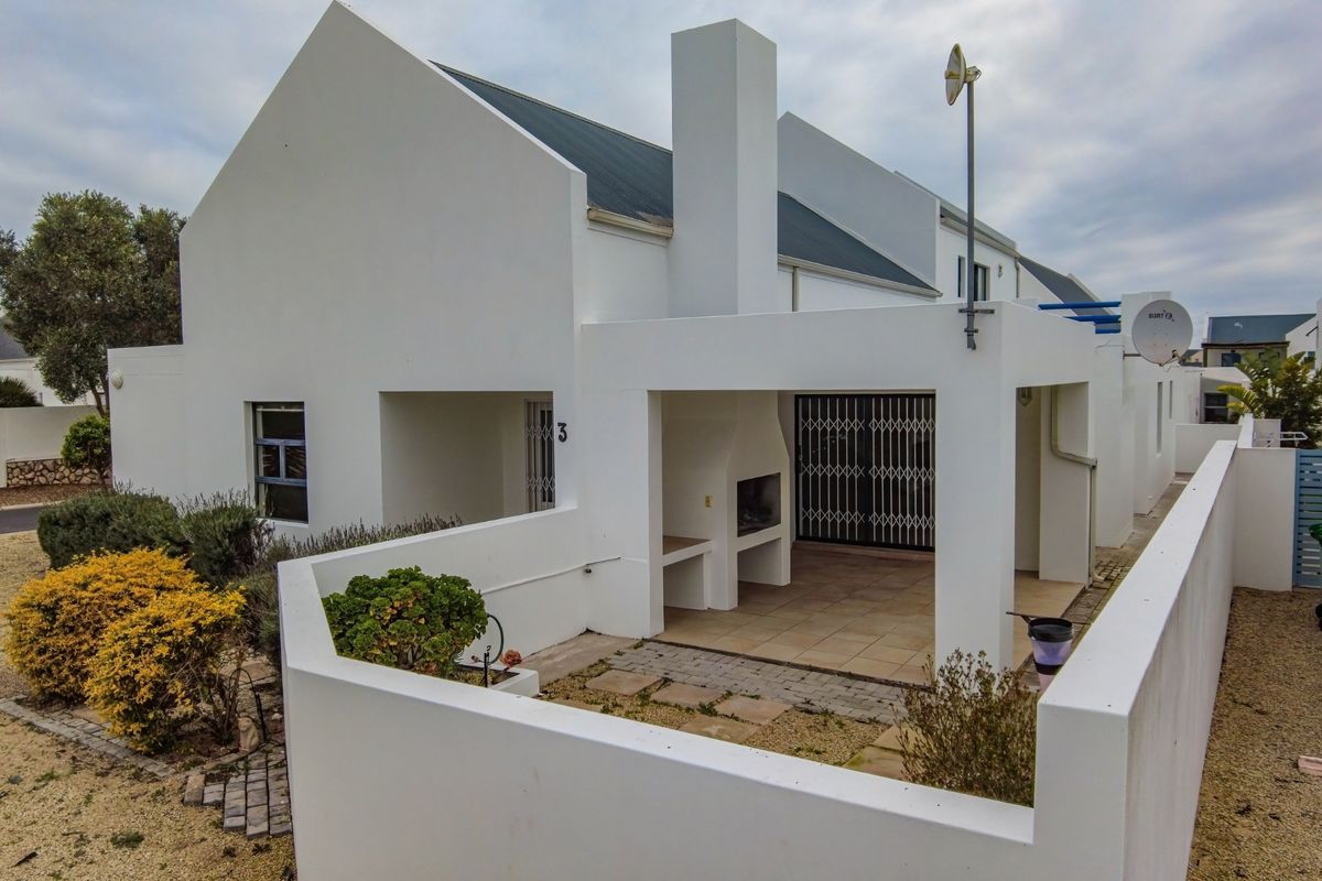 Rear view of the property featuring a covered patio with a built-in braai, white exterior walls, and a metal roof.