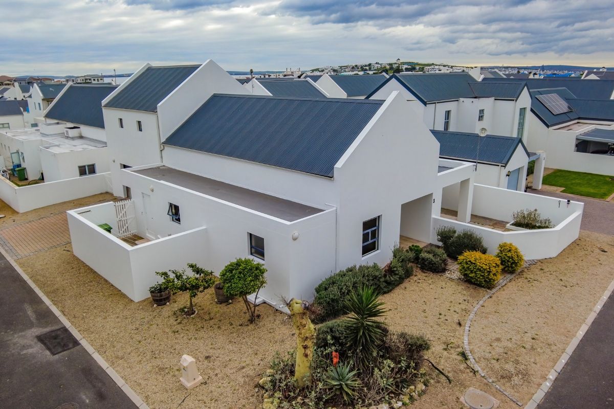 Aerial view of a modern residential property featuring a white facade, dark metal gabled roof, and surrounding landscaped garden area.