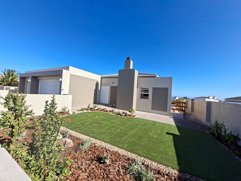 Rear view of the property featuring a landscaped garden with artificial lawn, paved patio area, timber decking, and a modern chimney stack.