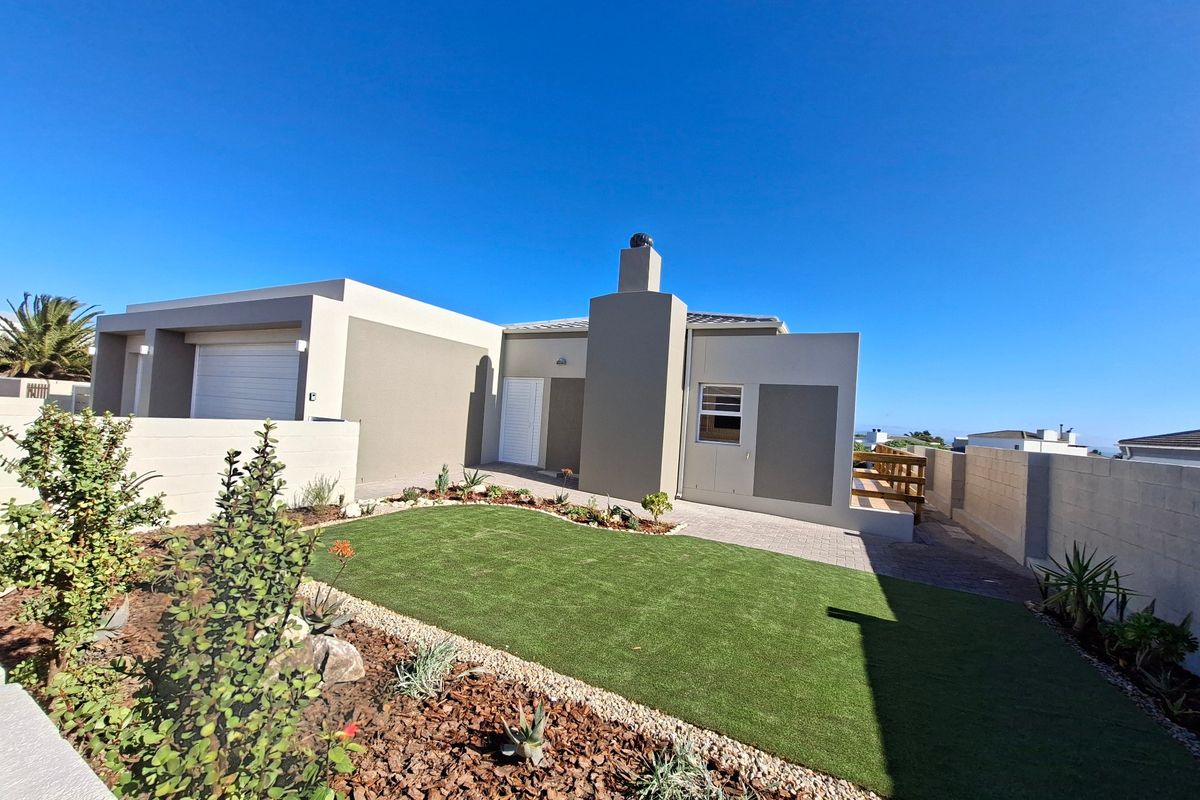 Rear view of the property featuring a landscaped garden with artificial lawn, paved patio area, timber decking, and a modern chimney stack.