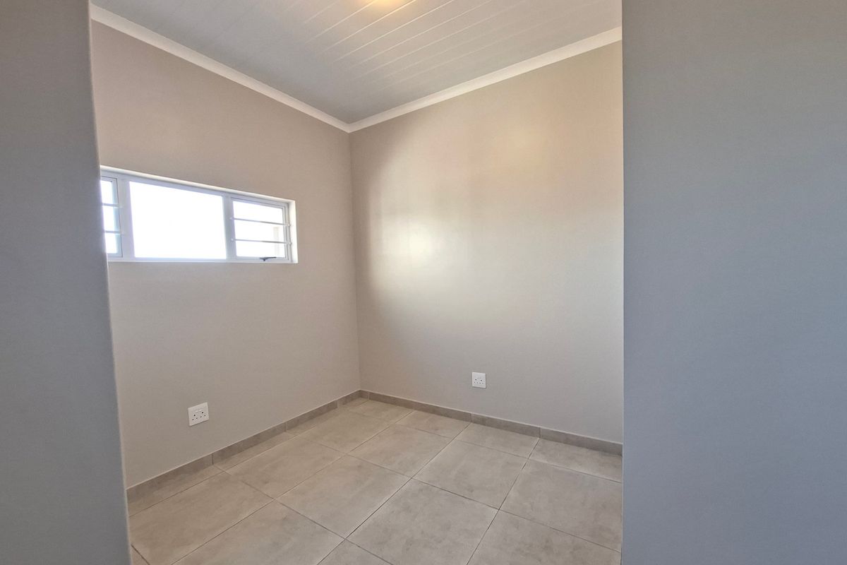 A clean, empty bedroom featuring neutral wall paint, tiled flooring, and a tongue and groove ceiling with a horizontal window.