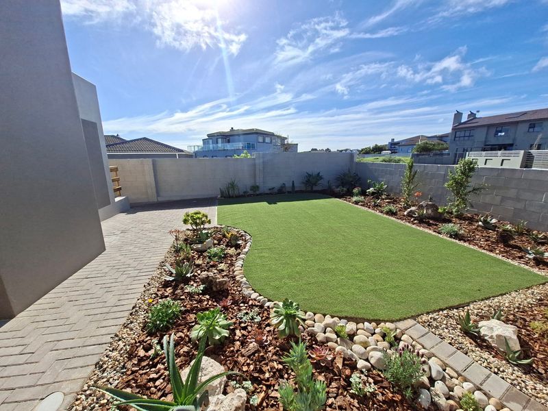 A well-maintained rear garden featuring a paved walkway, artificial lawn, and landscaped garden beds enclosed by a solid boundary wall.