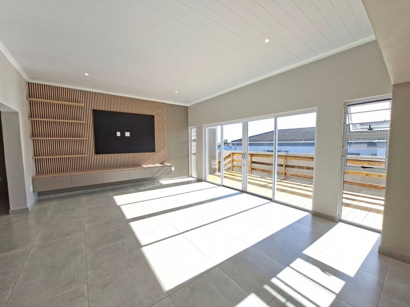 Spacious living area featuring a modern slatted timber feature wall, built-in cabinetry, large format floor tiles, and direct access to an outdoor deck.