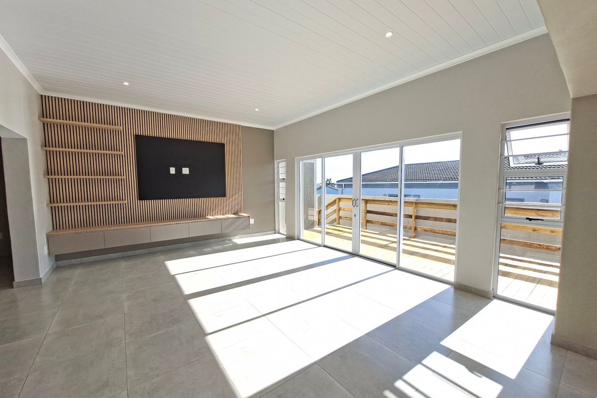Spacious living area featuring a modern slatted timber feature wall, built-in cabinetry, large format floor tiles, and direct access to an outdoor deck.