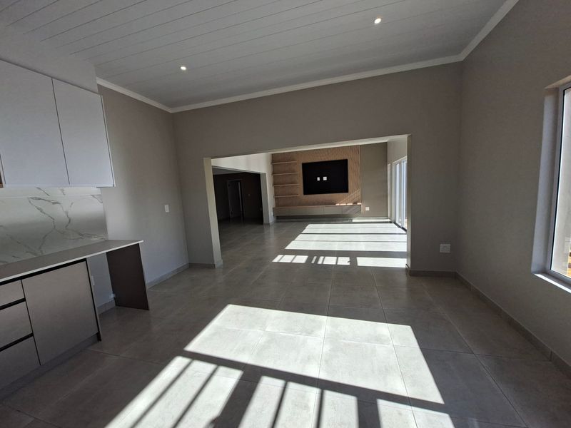Spacious open-plan living area featuring modern tiled floors, a sleek kitchen section, and a custom timber-accented media wall with recessed lighting.