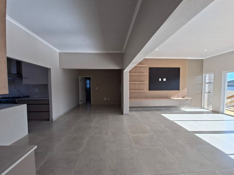 Spacious open-plan living area featuring modern tiled floors, a stylish slatted timber feature wall with built-in cabinetry, and an adjacent kitchen space.