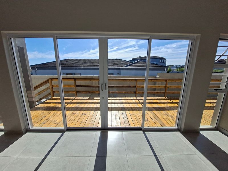 A bright, empty interior space featuring large sliding glass doors that open onto a wooden deck with a timber balustrade.