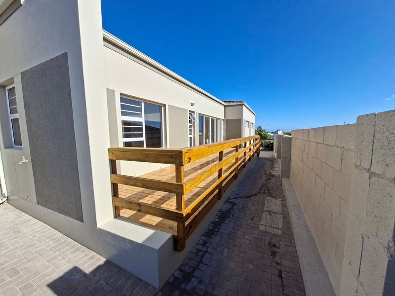 A well-maintained timber deck patio area featuring a wooden balustrade, paved side walkway, and direct access to the home via sliding glass doors.