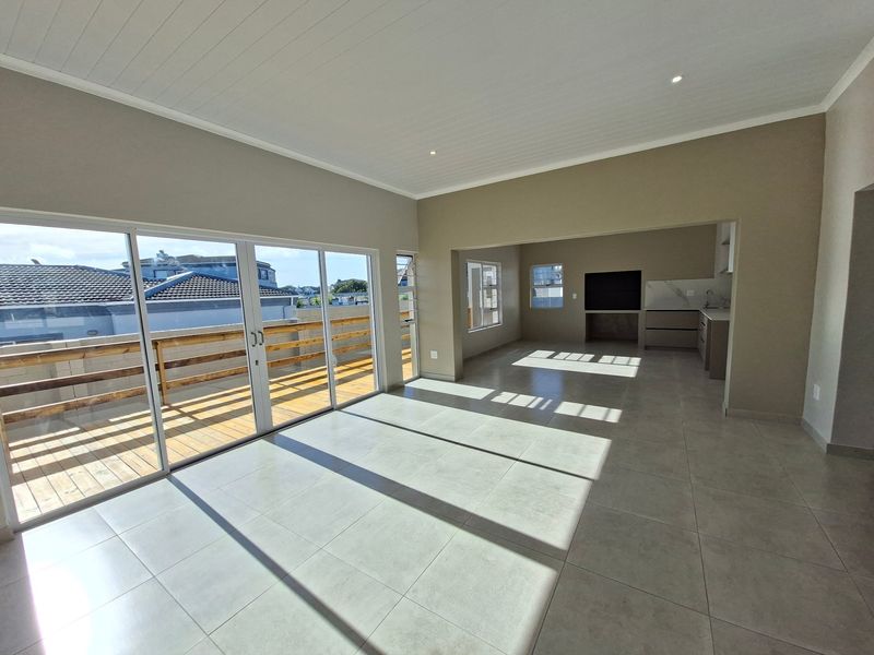 Spacious open-plan living area featuring large sliding doors leading to a timber deck, modern tiled floors, and a sleek integrated kitchen space.