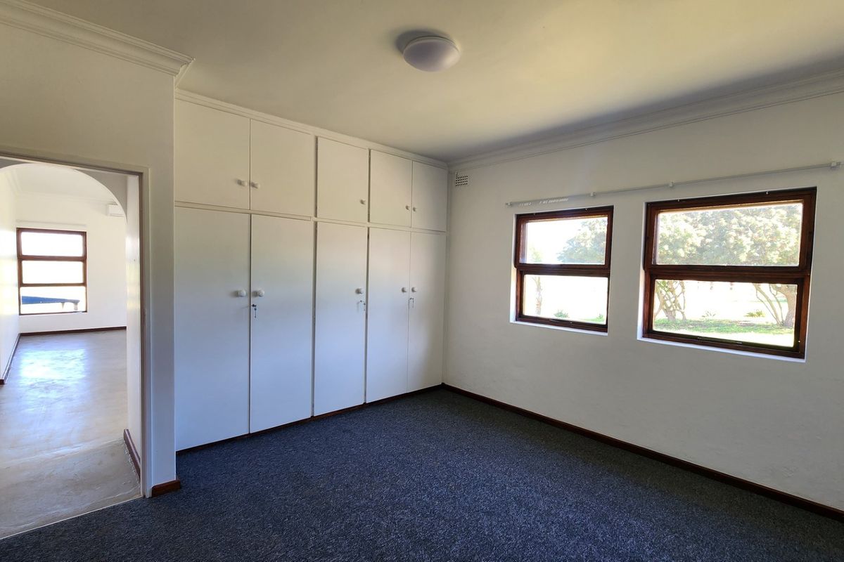 A spacious, empty bedroom featuring neutral walls, carpet flooring, and extensive built-in cupboard storage with an adjoining hallway.