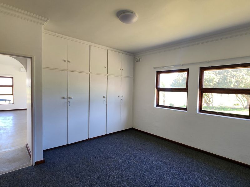 A spacious, empty bedroom featuring neutral walls, carpet flooring, and extensive built-in cupboard storage with an adjoining hallway.