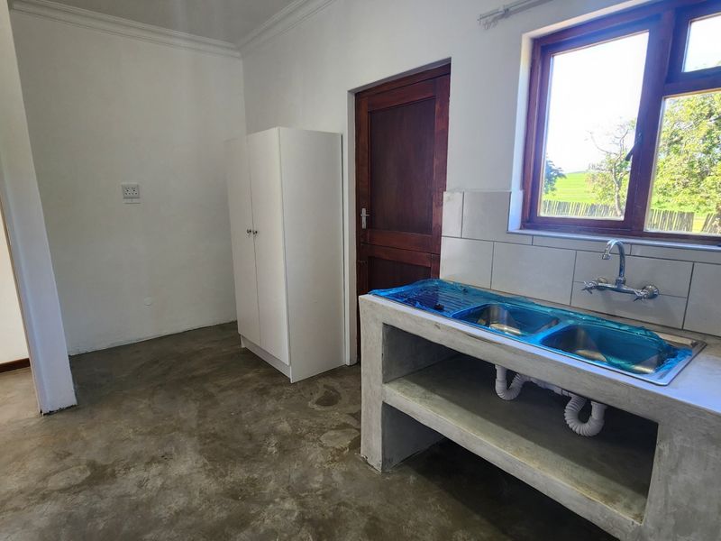 A functional kitchen area featuring a concrete countertop with a double sink, tiled splashback, and direct access to the exterior.