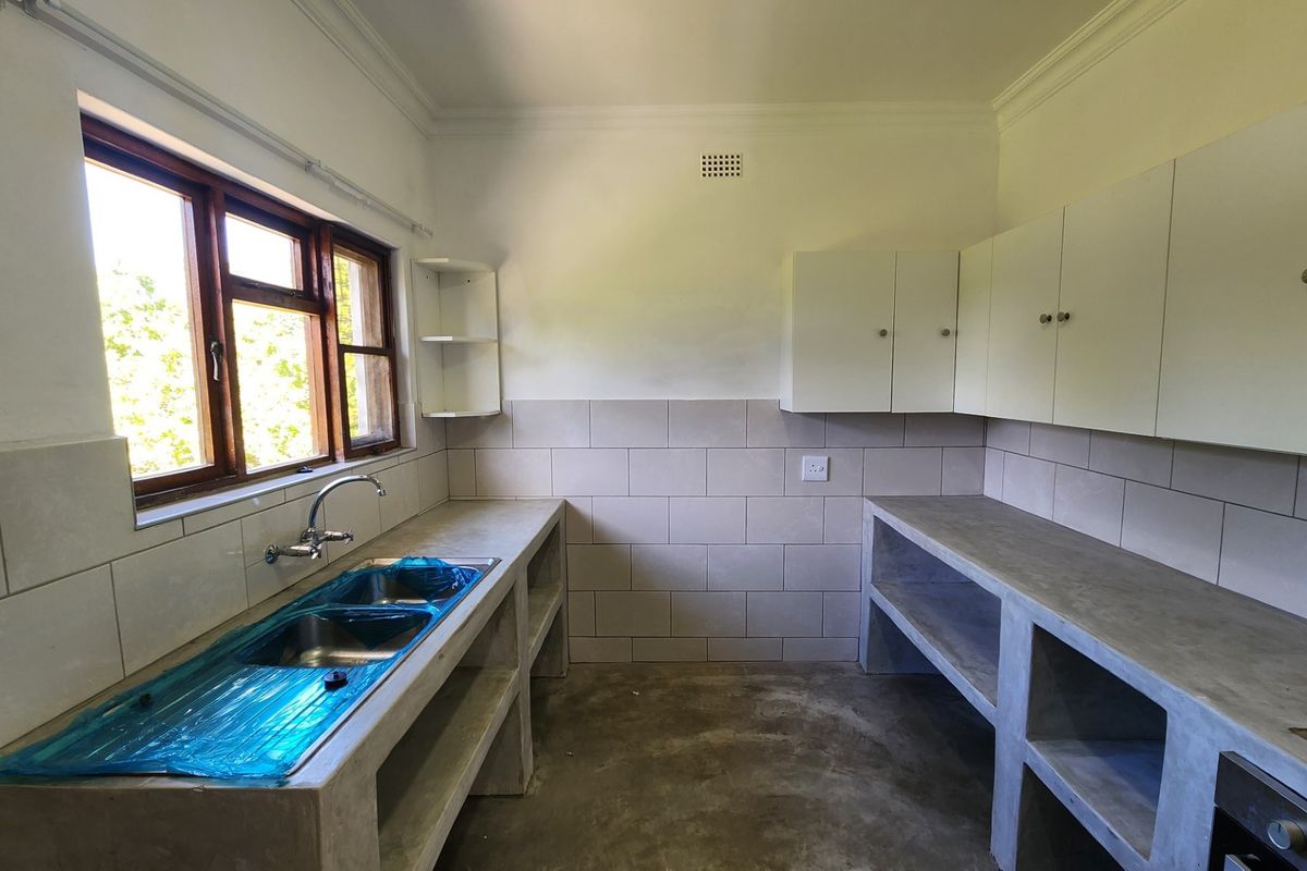 A functional kitchen space featuring concrete countertops, a double basin sink, tiled backsplash, and built-in cabinetry, currently in an unfinished state.